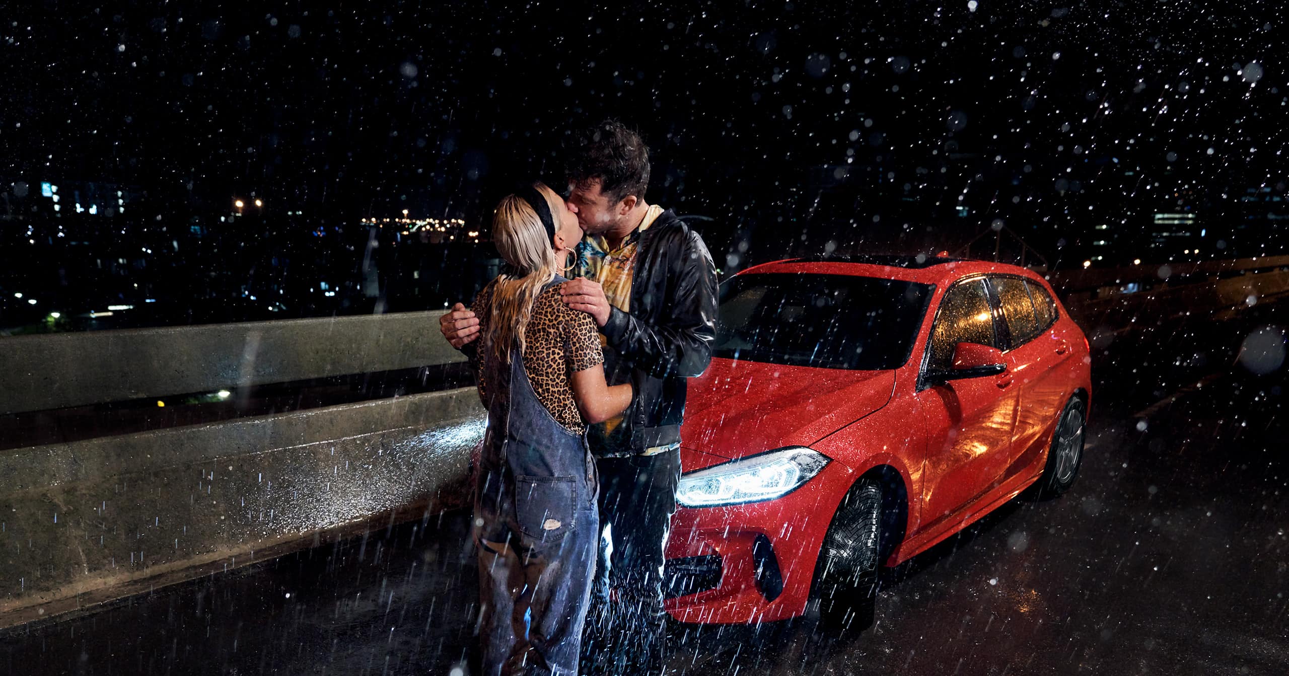 Par kysser foran en rød bil med helårsdæk